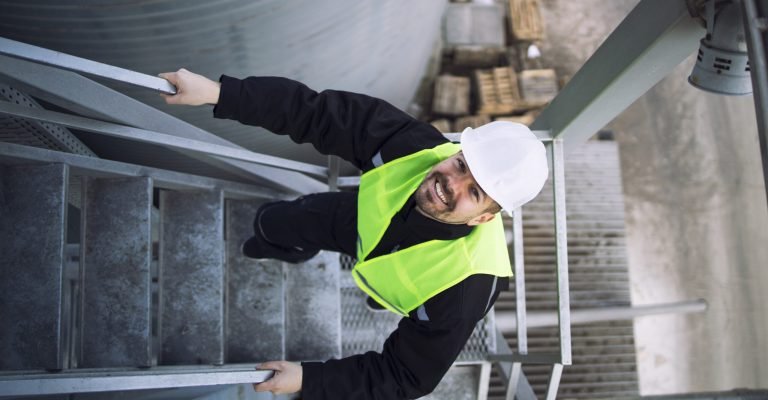 Top view of factory worker climbing metal stairs on industrial silo building. Top view of factory worker climbing metal stairs on industrial silo building.